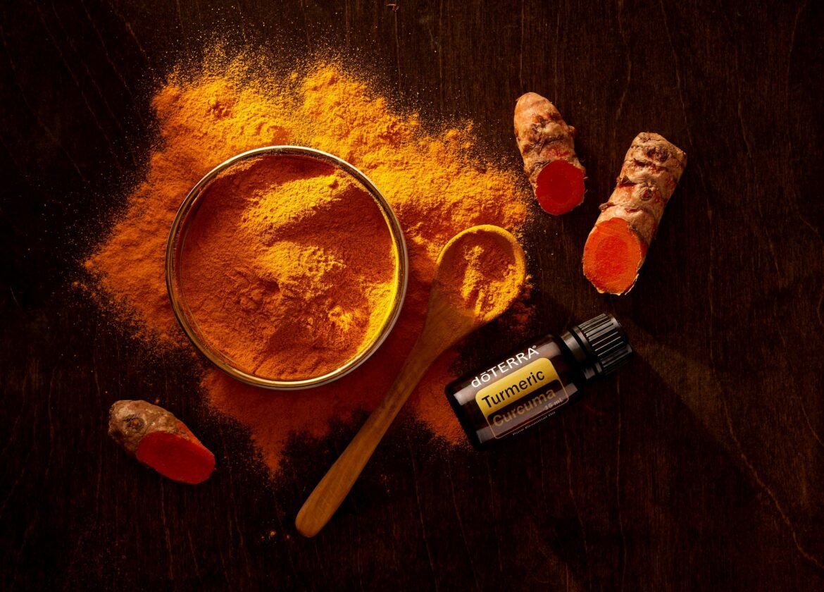 Top view of turmeric powder, curcuma roots, and essential oil on wooden surface.