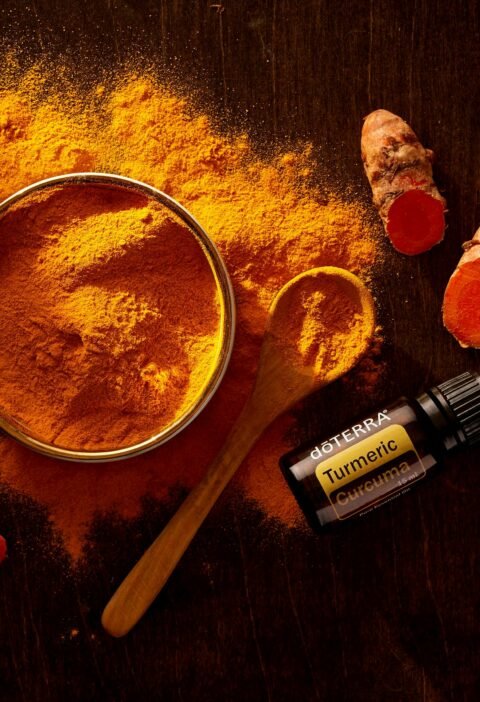 Top view of turmeric powder, curcuma roots, and essential oil on wooden surface.