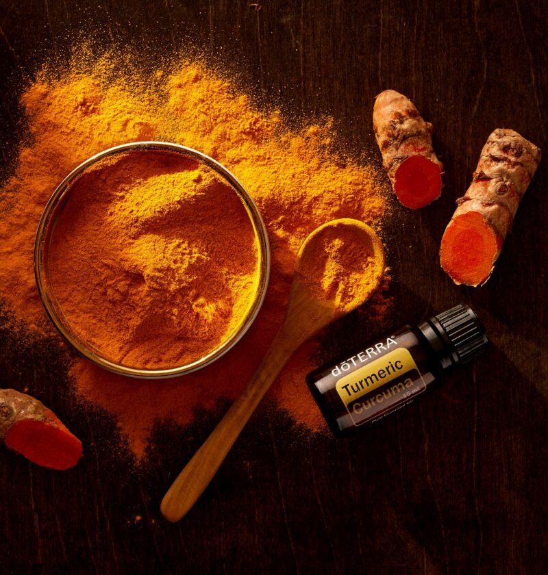 Top view of turmeric powder, curcuma roots, and essential oil on wooden surface.