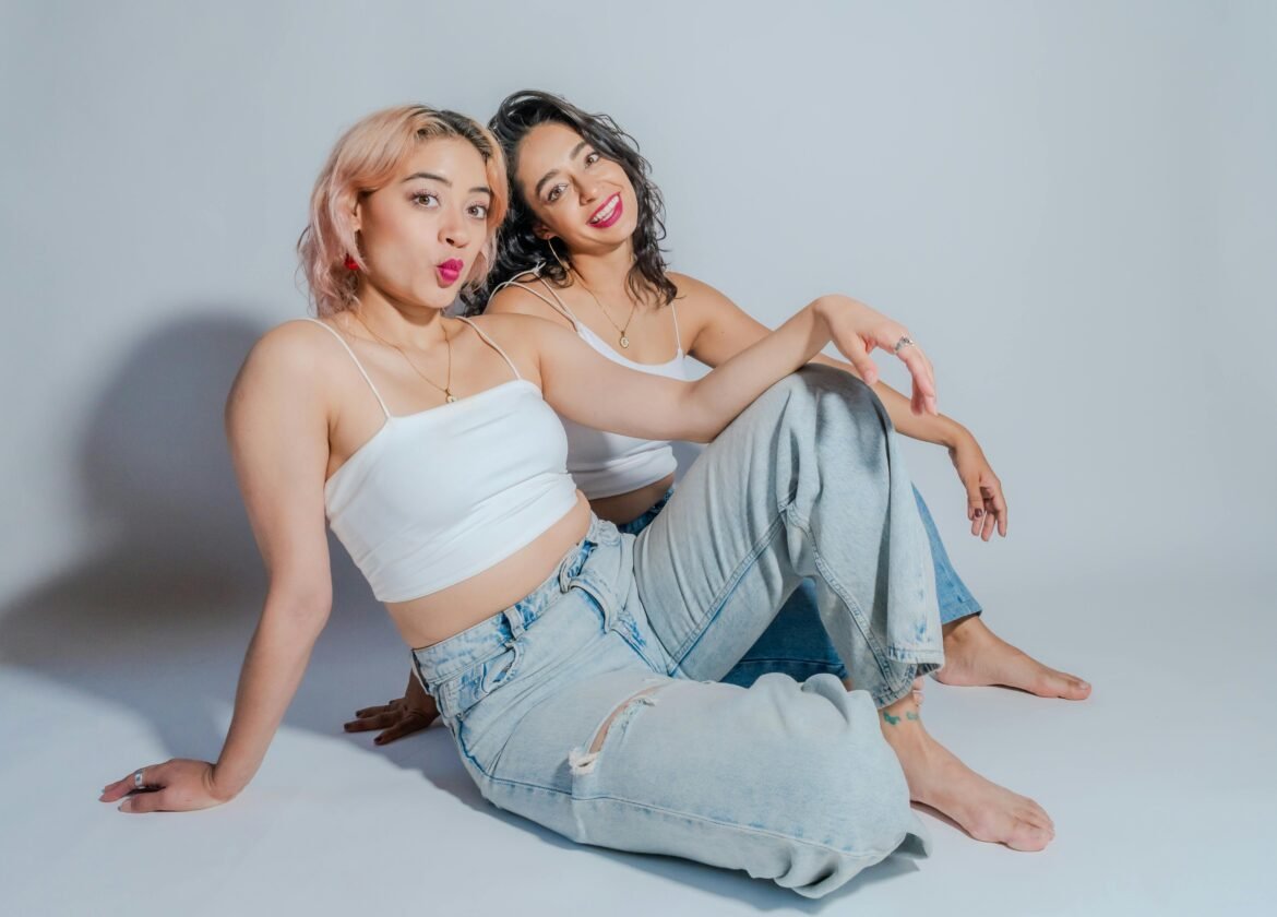 Two young women in casual attire sit together, showcasing friendship and style.