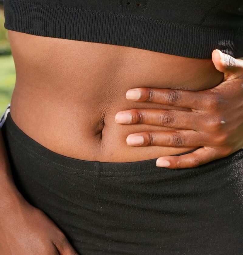 Close-up of a person holding their abdomen, indicating stomach discomfort, outdoors.