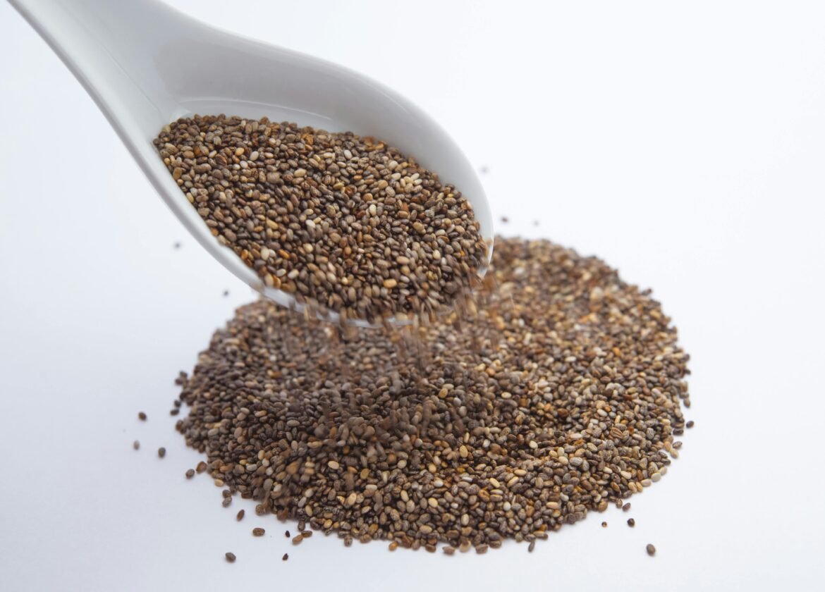 A close-up shot of chia seeds pouring from a white ceramic spoon onto a white surface.
