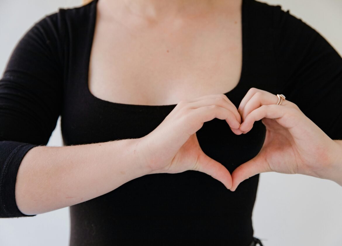 Close-up of a woman's hands making a heart gesture, symbolizing love.