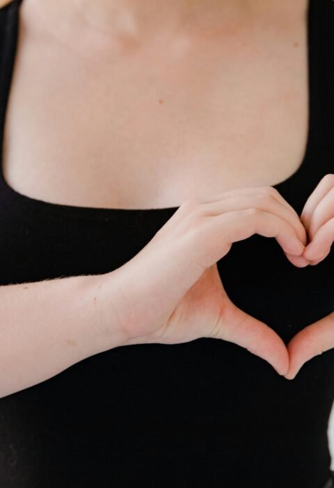 Close-up of a woman's hands making a heart gesture, symbolizing love.