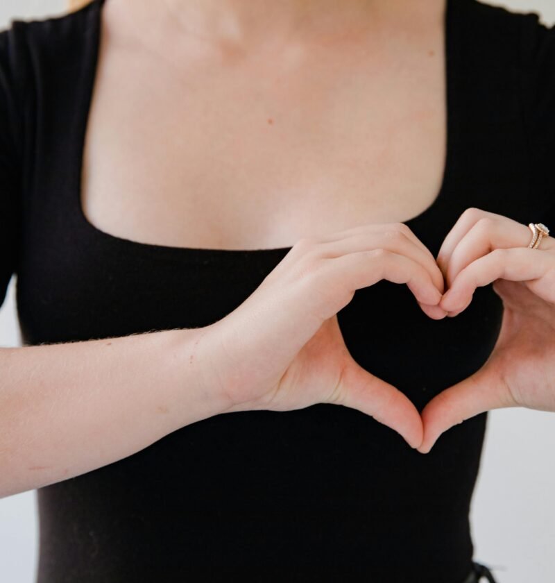 Close-up of a woman's hands making a heart gesture, symbolizing love.