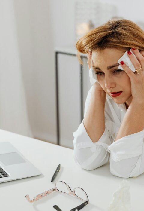 A woman in distress at her office desk, surrounded by tissues and a laptop.